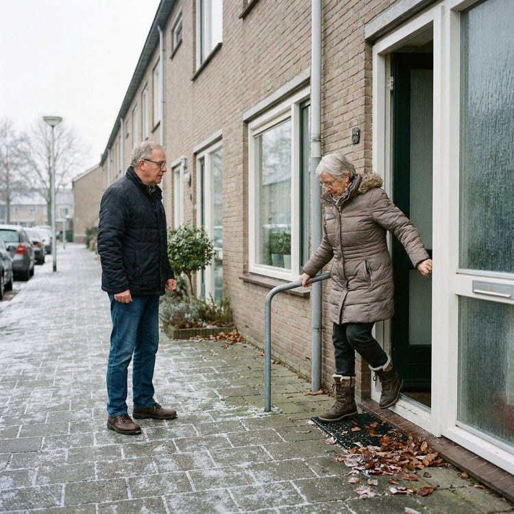 Oudere vrouw loopt voorzichtig met boodschappentas over een licht beijzelde stoep bij haar woning, terwijl een buur klaarstaat om te helpen.